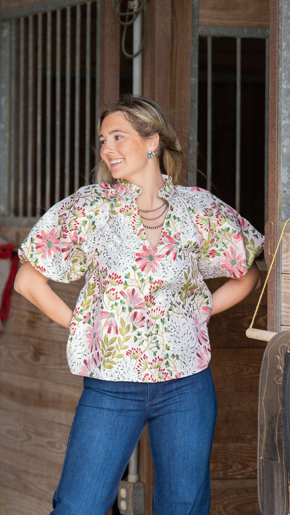 Woman wearing a floral blouse and blue jeans standing in front of wooden stable doors.