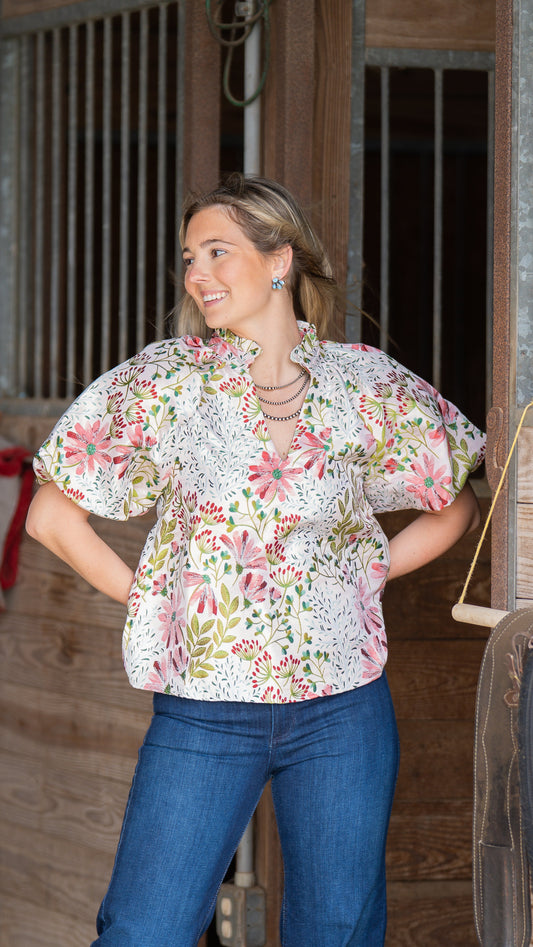 Woman wearing a floral blouse and blue jeans standing in front of wooden stable doors.
